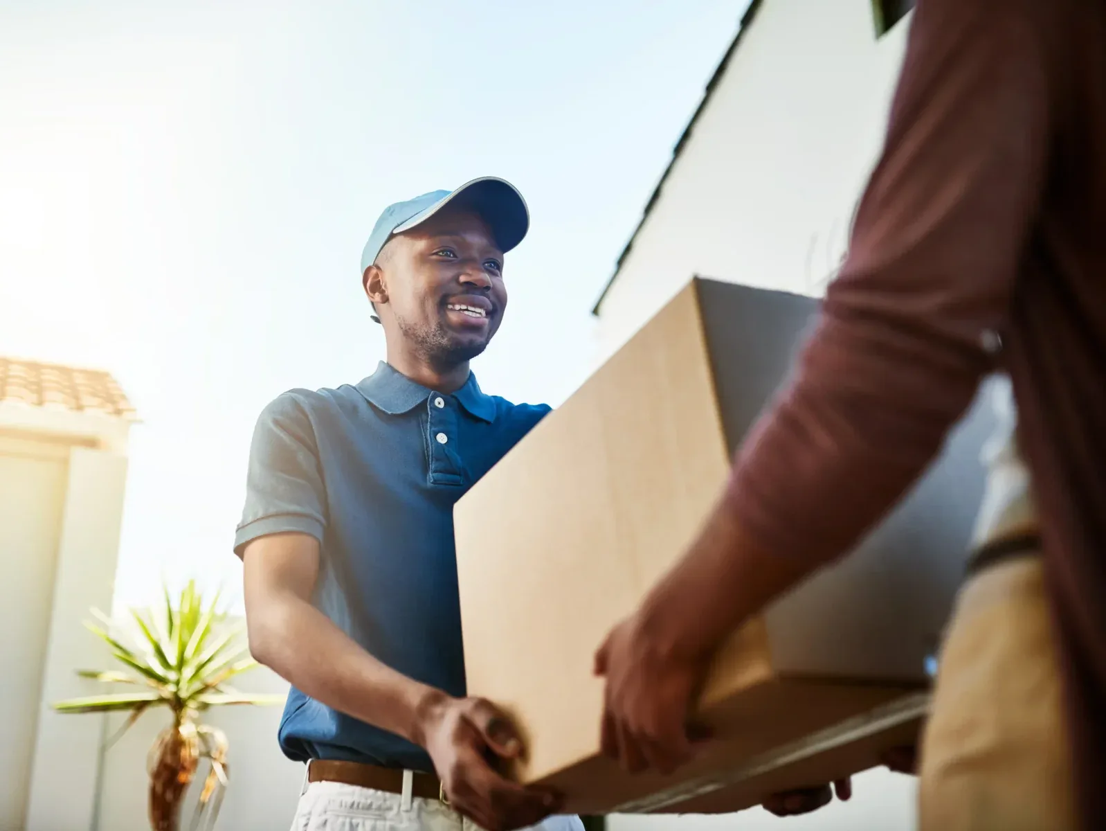 A delivery person in a blue shirt and cap hands a large cardboard box to another person outside a building, showcasing the reliable service offered by Brightside Moving Group for big moves and long-distance moving services.